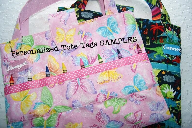 May include: Two personalized tote bags with butterfly patterns. One bag is pink with a butterfly pattern and has a name tag that says "Gwenyth". The other bag is black with a dinosaur pattern and has a name tag that says "Conner". Both bags have a ribbon with white polka dots and are labeled "Personalized Tote Tags SAMPLES".