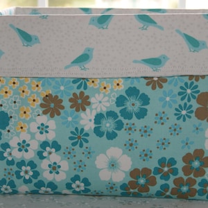 May include: A blue and white fabric storage bin with a floral pattern. The bin has a white top with blue birds and a blue bottom with a floral pattern.