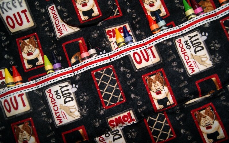 May include: A black fabric organizer with red and white trim. The organizer has multiple pockets with various images of dogs and the text "Watchdog on Duty" and "Keep Out". Crayons are stored in the pockets.