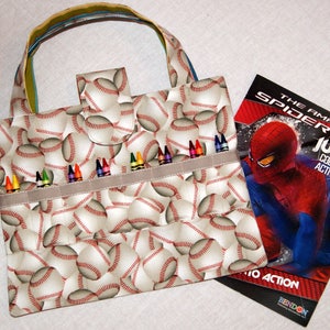 May include: A white canvas tote bag with a baseball print. The bag has a pocket on the front and a zippered compartment on the top. The bag is filled with crayons. A coloring book with a Spiderman character on the cover is next to the bag. The coloring book title is "The Amazing Spider-Man Junior Coloring Activity Book".