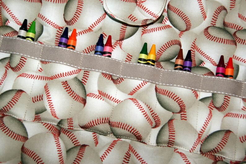 May include: A gray fabric pouch with a white and red baseball pattern. The pouch has a gray ribbon across the top with a row of colored crayons inserted into the ribbon.