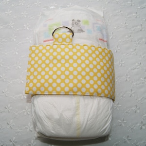 May include: A white diaper with a yellow and white polka dot fabric diaper cover. The cover has a metal ring for hanging.
