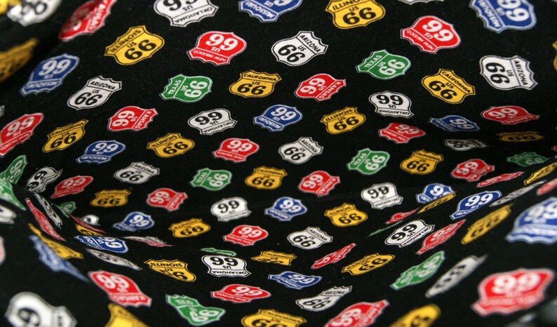 May include: Black fabric with a repeating pattern of colorful Route 66 and Route 99 highway signs. The signs are in various states, including Arizona, California, Illinois, Missouri, and Texas.