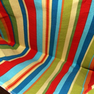 May include: A close-up of the inside of a striped fabric bag. The fabric is a mix of red, blue, yellow, and green stripes.