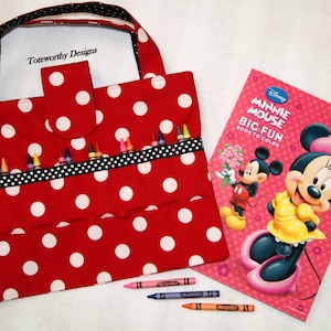 May include: Red and white polka dot fabric tote bag with a black and white ribbon and a pocket on the front. The bag is filled with crayons and a coloring book featuring Minnie Mouse and Mickey Mouse. The coloring book cover says "Minnie Mouse Big Fun Book to Color".