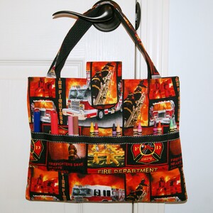 Könnte beinhalten: Eine schwarze Stofftasche mit Feuerwehr- und Feuerwehrmann-Motiv. Die Tasche hat mehrere Fächer und ist perfekt zum Transport von Buntstiften, Markern und anderen Bastelutensilien. Die Tasche trägt den Schriftzug "Fire Fighters" und "Fire Department".