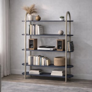 Op de afbeelding: Een moderne boekenplank met vier marineblauwe planken en goudkleurige steunen. De planken tonen boeken, een platenspeler, luidsprekers en decoratieve items. Een plant en een raam zijn zichtbaar op de achtergrond.