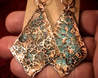 May include: A pair of handcrafted copper earrings with a textured, diamond-like shape. The earrings feature a hammered design with turquoise-colored accents, and are suspended from copper ear wires. The earrings are displayed against a neutral background.