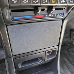 Puede incluir: Primer plano del salpicadero de un coche con un panel de control negro y gris. El panel tiene botones para el aire acondicionado, la calefacción y la ventilación. También hay botones para ajustar la temperatura y la velocidad del ventilador. El panel tiene una pantalla digital que muestra la temperatura y la velocidad del ventilador. El panel está hecho de plástico y tiene una superficie texturizada.
