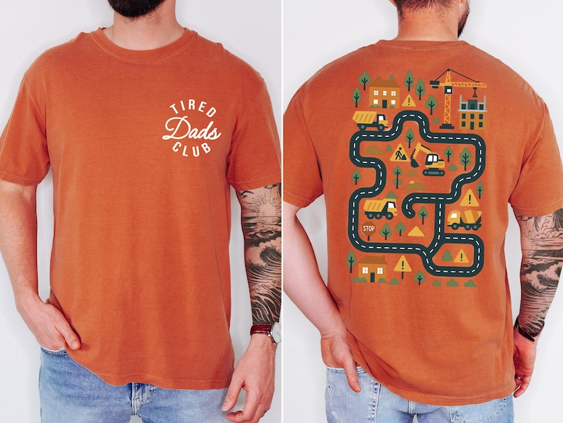 May include: Burnt orange t-shirt with "Tired Dads Club" text on the front. The back features a construction-themed graphic with roads, buildings, and construction vehicles. A fun, casual tee for dads.