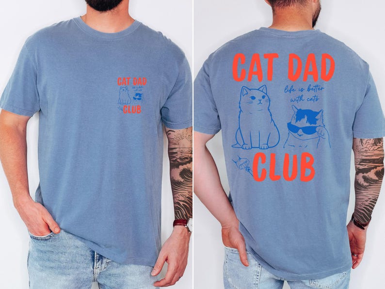 May include: Blue short-sleeved t-shirt with the text "CAT DAD CLUB" in orange. The front features a cat graphic, and the back has two cat illustrations and the phrase "life is better with cats."