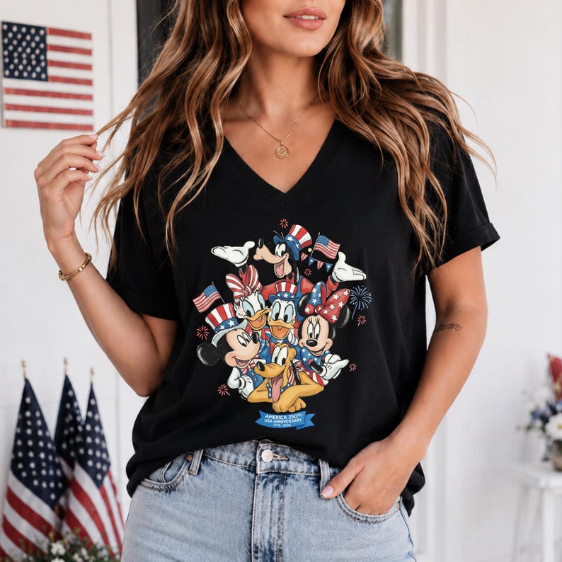 Może przedstawiać: Czarny t-shirt z dekoltem w serek z grafiką postaci Disneya w patriotycznych strojach, w tym Myszki Miki i Myszki Minnie, Kaczora Donalda i Kaczki Daisy oraz Pluto. Projekt zawiera amerykańskie flagi i fajerwerki. Tekst brzmi "America 1776 Anniversary".