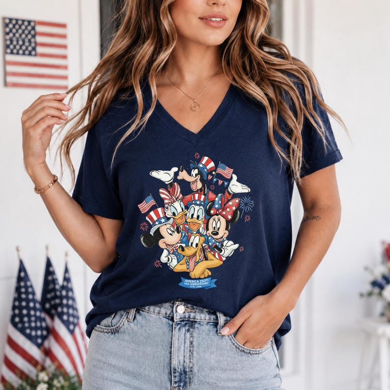 Może przedstawiać: Granatowa koszulka z dekoltem w serek z patriotycznym wzorem z Myszką Miki, Myszka Minnie, Kaczorem Donaldem, Daisy Duck i Pluto. Postacie trzymają amerykańskie flagi i noszą patriotyczne akcesoria. Koszulka ma napis "America 250th USA Anniversary".