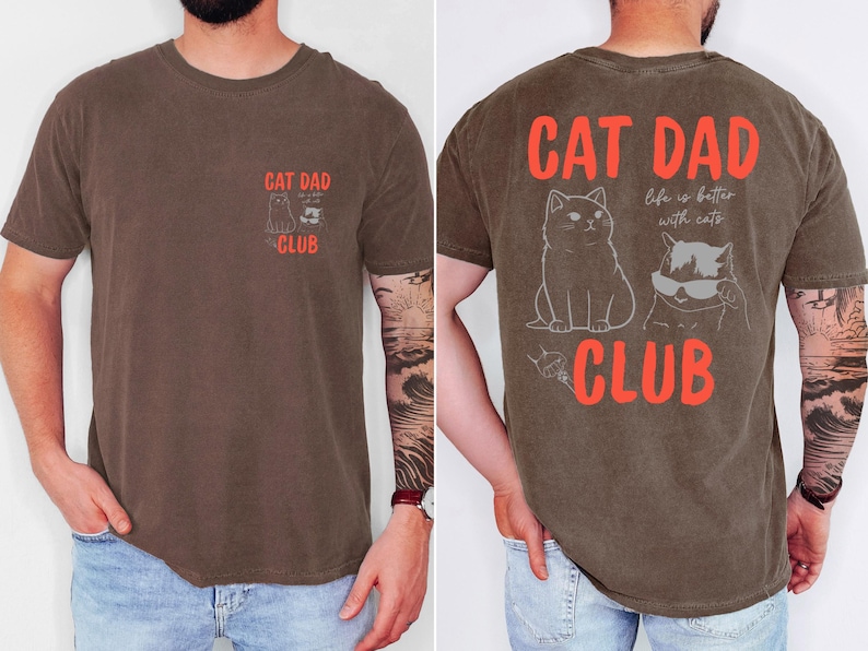 May include: Brown t-shirt with the text "CAT DAD CLUB" in red. The front of the shirt has a small graphic of a cat and the text "CAT DAD CLUB". The back of the shirt features two cat illustrations and the phrase "life is better with cats".