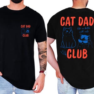 May include: Black t-shirt with the text "CAT DAD CLUB" in red and blue. The front features a small graphic, while the back displays two cat illustrations and the phrase "life is better with cats."