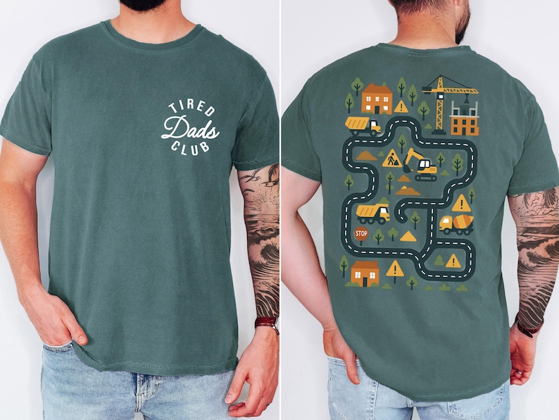 May include: A teal-colored t-shirt with the text "Tired Dads Club" in a white, circular design on the front. The back features a construction-themed graphic with trucks, a crane, and a road map design.