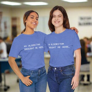 May include: Two people wearing matching blue t-shirts with the text "MY ALGORITHM BROUGHT ME HERE" in white. They are smiling and wearing blue jeans. The background is a blurred interior.