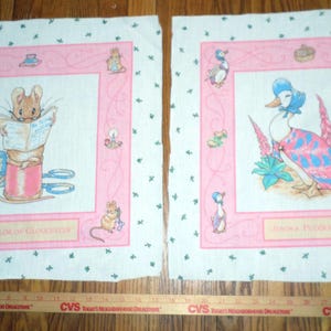 May include: Two pink and white fabric squares with a pink border and a white background. The left square features a mouse holding a book with the text "The Tailor of Gloucester". The right square features a blue duck with a pink and blue patterned dress and the text "Jemima Puddle-Duck".