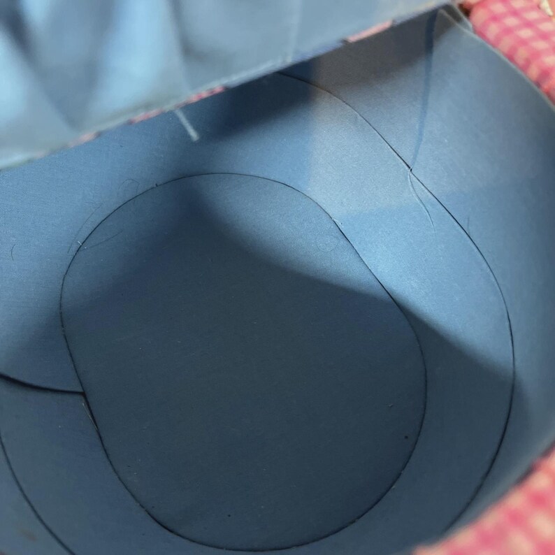 May include: An inside view of a blue paper container with curved edges. The container has a circular base and is partially open, revealing a pink and white patterned edge. The lighting creates shadows.
