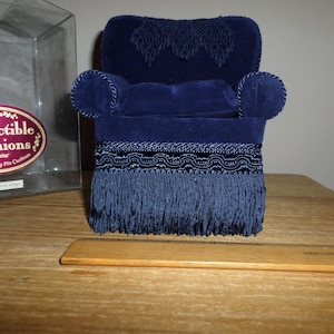 May include: A blue velvet armchair with a fringe trim and a label that reads "Collectible Cushions by Delta Exquisite Novelty Pin Cushions".