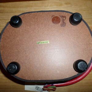 May include: Oval-shaped wooden tray with four black, rounded feet. The tray's underside is brown with a label that reads "MADE IN PHILIPPINES". The rim is red with a black trim.