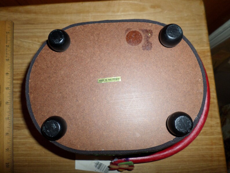 May include: Oval-shaped wooden tray with four black, rounded feet. The tray's underside is brown with a label that reads "MADE IN PHILIPPINES". The rim is red with a black trim.