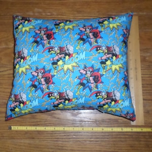 May include: A blue pillow with a repeating pattern of Thor, the Norse god of thunder, wielding his hammer, Mjolnir. The pattern also includes the word "THOOOM" in yellow and white.