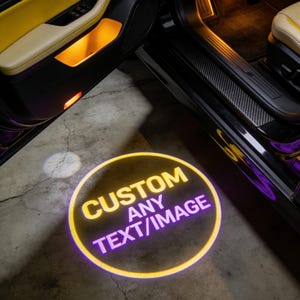 May include: A custom car door projector displaying a circular design with the words "CUSTOM ANY TEXT/IMAGE" in yellow and purple. The car door is open, revealing the interior with yellow and black accents.