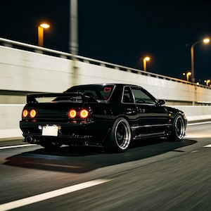 Op de afbeelding: Een zwarte sportwagen met een achterspoiler en rode achterlichten rijdt 's nachts op een snelweg. Een hartvormige sticker is zichtbaar op de achterruit. De weg wordt verlicht door straatverlichting.