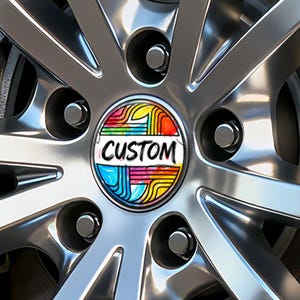 May include: Close-up of a shiny, silver car wheel with a colourful centre cap. The centre cap features the word "CUSTOM" in white, surrounded by a vibrant design of rainbow-coloured lines and shapes. The wheel has multiple spokes and lug nuts.