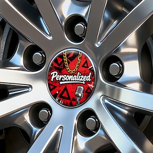 Puede incluir: Una llanta de coche cromada con un tapacubos personalizado. El tapacubos rojo presenta una cadena dorada, un micrófono y la palabra "Personalized" en blanco. El diseño incluye triángulos y formas negras.