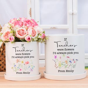 Puede incluir: Dos macetas de cerámica blanca con platillos, cada una adornada con el texto "If Teachers were flowers I'd always pick you" y un diseño floral. Una maceta contiene flores rosas. El texto "From Emily" está en la parte inferior.