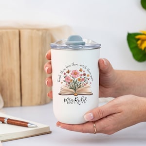 Pu&ograve; includere: Bicchiere termico bianco con coperchio grigio, tenuto in mano da una persona. Il bicchiere presenta un motivo floreale con un libro aperto e il testo "Teach them, love them, watch them grow" e "Mrs. Rachel". Una penna e un taccuino sono sullo sfondo.