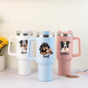May include: Three stainless steel tumblers with handles and straws. The white tumbler features a dog and the name Noah. The light blue tumbler shows a puppy and kitten with the name Kent. The dusty pink tumbler displays a dog and the name Carter.