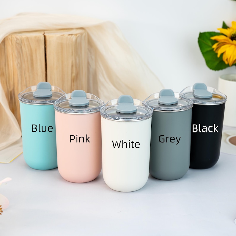 Pu&ograve; includere: Cinque bicchieri isolanti blu, rosa, bianchi, grigi e neri, ciascuno con un coperchio trasparente e una chiusura a ribalta grigia. I colori sono etichettati sulla parte anteriore di ogni bicchiere. I bicchieri sono cilindrici e sembrano essere in metallo.