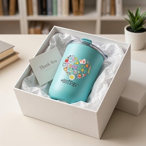Pu&ograve; includere: Un bicchiere termico turchese con un design a forma di cuore con icone scolastiche e la scritta "Hello Teacher Mrs. Trista". Il bicchiere &egrave; in una confezione regalo bianca con un biglietto "Thank You".