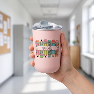Pu&ograve; includere: Un bicchiere termico rosa con coperchio trasparente e chiusura a ribalta grigia. Il bicchiere presenta un colorato disegno di matite con la scritta "Mrs. Cathy". Le matite hanno vari motivi e colori, tra cui arancione, rosa, verde e blu.