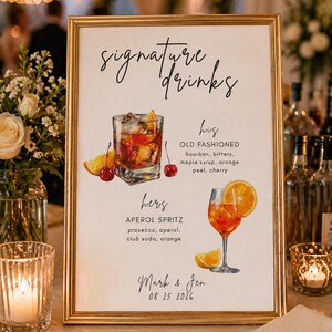 Puede incluir: Un letrero enmarcado en dorado con las palabras "signature drinks". El letrero detalla dos recetas de cócteles: un Old Fashioned y un Aperol Spritz, con los nombres "his" y "hers". El letrero está personalizado con los nombres "Mark & Jen" y la fecha "08 25 2026".