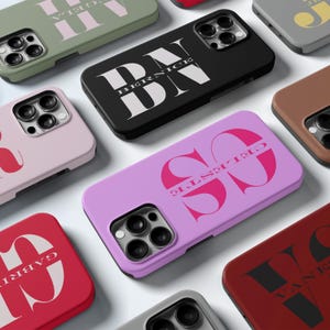 May include: A collection of personalised phone cases with various names and designs. The cases are in different colours, including black, pink, red, and green. The names on the cases are "Bernice", "SO", "Gabrielle", and "Van E".