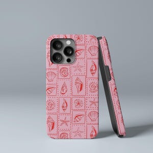 Puede incluir: Funda de teléfono rosa con un patrón repetido de conchas marinas rojas, estrellas de mar y otras criaturas marinas. El diseño está dispuesto en una cuadrícula de cuadrados tipo sello postal. Una segunda funda está apoyada al lado.