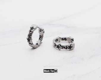 May include: Two silver hoop earrings with a star design and black detailing. The earrings are shown on a white surface. The text "Black Fox" is in a black rectangle.
