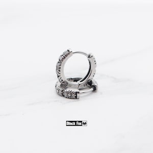 May include: Silver hoop earrings with a floral pattern. The earrings are made of a shiny metal and have a detailed design of small flowers around the hoops. The brand name "Black Fox" is in a black rectangle.
