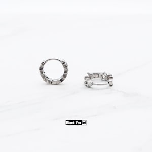 May include: Two silver hoop earrings with star-shaped cutouts. The earrings are displayed on a white marble surface. The brand name "Black Fox" is printed in a black rectangle.
