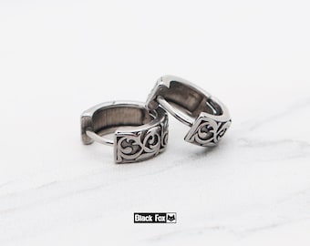 May include: Two silver hoop earrings with an intricate, swirling pattern. The earrings are presented on a white marble surface. The brand name "Black Fox" is printed in a black rectangle.