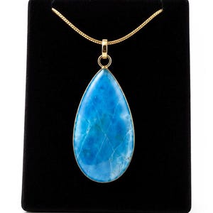 May include: A teardrop-shaped blue stone pendant with a gold-toned metal rim and bail, suspended from a matching gold-toned chain. The stone features natural white veining throughout its vibrant blue surface, creating a distinct pattern.