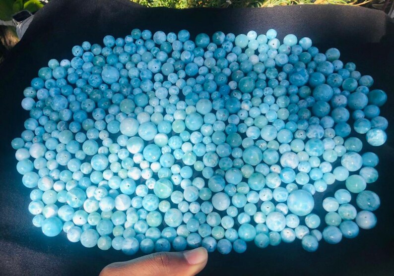 K&ouml;nnte beinhalten: Eine Ansammlung hellblauer, runder Perlen in verschiedenen Gr&ouml;&szlig;en. Die Perlen sind auf einer dunklen Oberfl&auml;che angeordnet und erzeugen einen strukturierten Effekt. Die Perlen scheinen aus einem durchscheinenden Material zu bestehen.