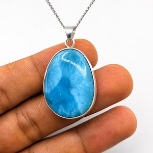 May include: A teardrop-shaped larimar pendant set in a polished silver bezel, suspended from a delicate silver chain. The stone features a vibrant sky-blue color with intricate, cloud-like white patterns throughout its smooth, polished surface.