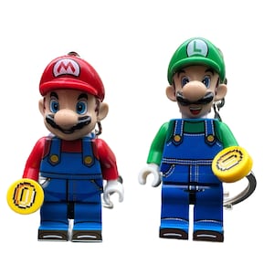 May include: Two keyrings depicting Mario and Luigi from Super Mario Bros. Mario wears a red cap and Luigi a green cap. Both figures have blue overalls and hold a yellow coin.