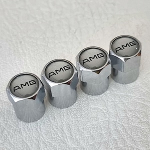 May include: Four silver-colored tire valve caps with the word "AMG" printed in black on each cap.