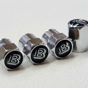 Può includere: Quattro tappi per valvole di pneumatici argentati con un logo "B" nero.